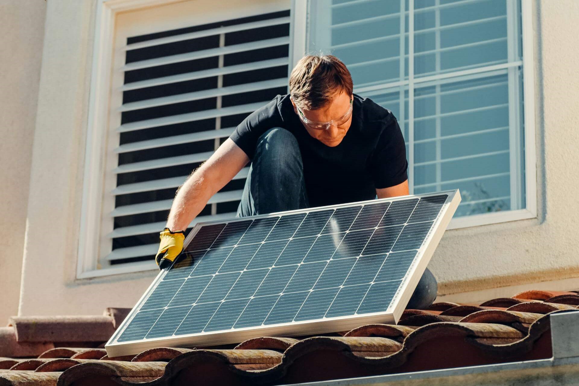 Man installing solar panel on roof of house